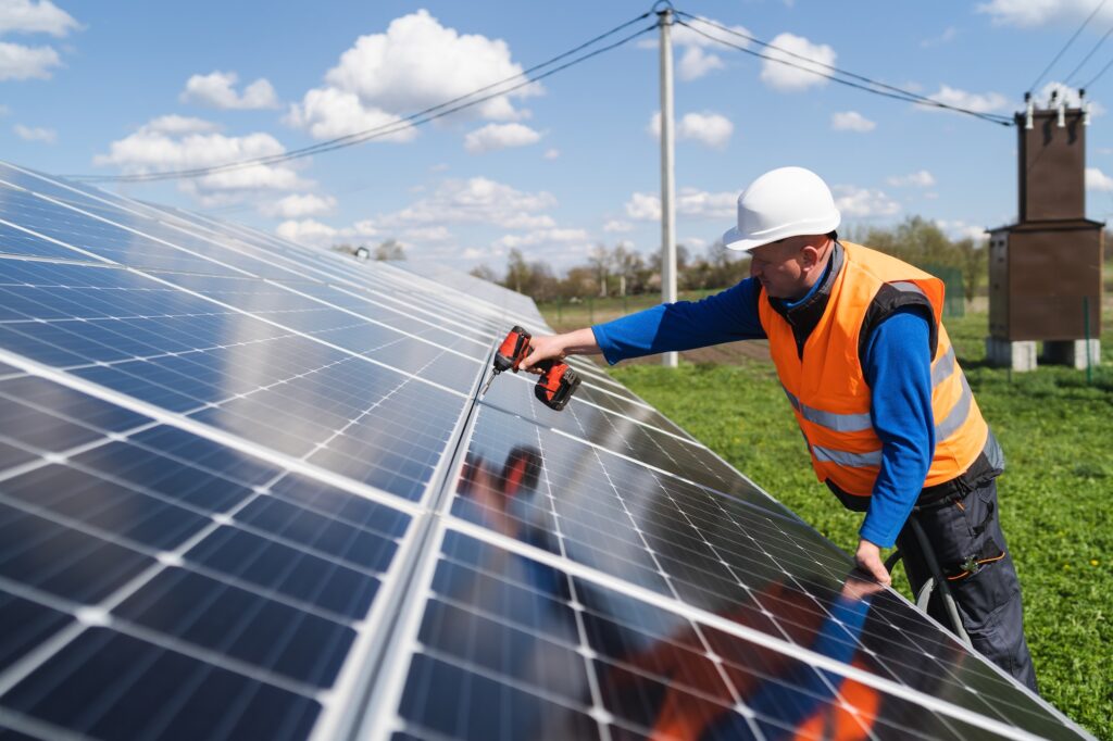 Man with drill screwdriver installs panels at a solar power plant